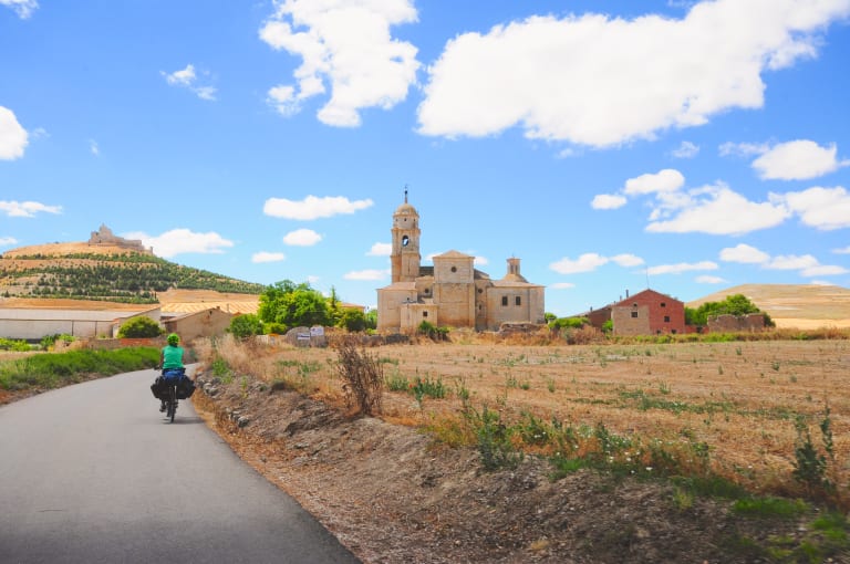Ciclista lungo una strada nel percorso per Santiago con un monastero medioevale sullo sfondo